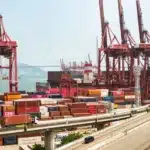 A vibrant view of Hong Kong's bustling shipping port with red cranes and stacked containers.