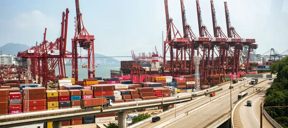 A vibrant view of Hong Kong's bustling shipping port with red cranes and stacked containers.