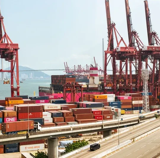 A vibrant view of Hong Kong's bustling shipping port with red cranes and stacked containers.