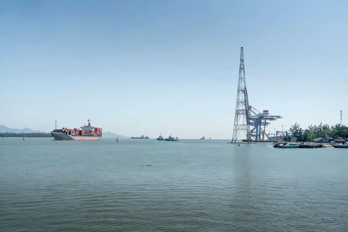 A large container ship sails through an industrial harbor under a clear sky, showcasing maritime log